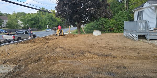 Construction workers preparing soil near a house with a tree in the yard.