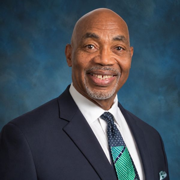 Smiling man in a suit with a patterned tie against a blue background.