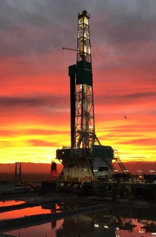 Illuminated oil rig tower at sunset with vibrant orange sky.
