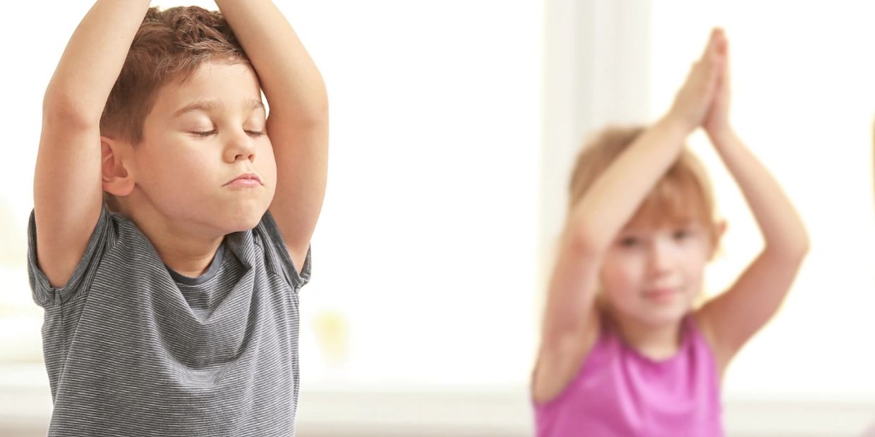 Two children practicing yoga with eyes closed and hands raised.