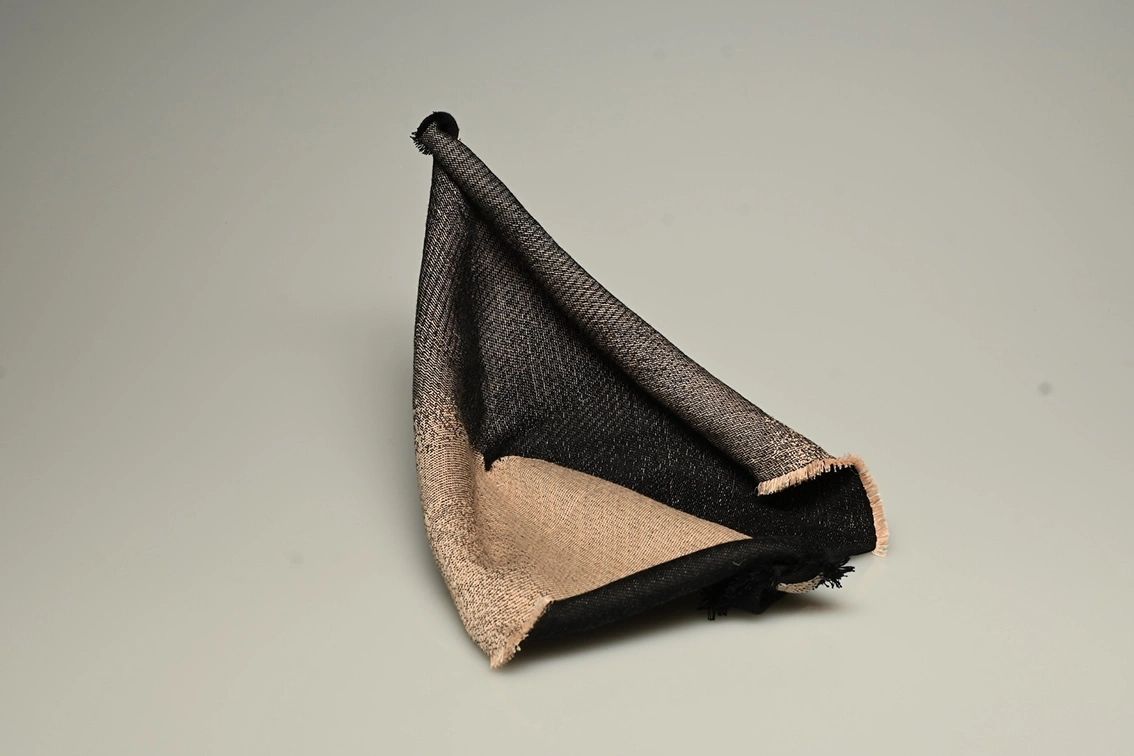A folded two-tone black and beige woven fabric on a plain surface.