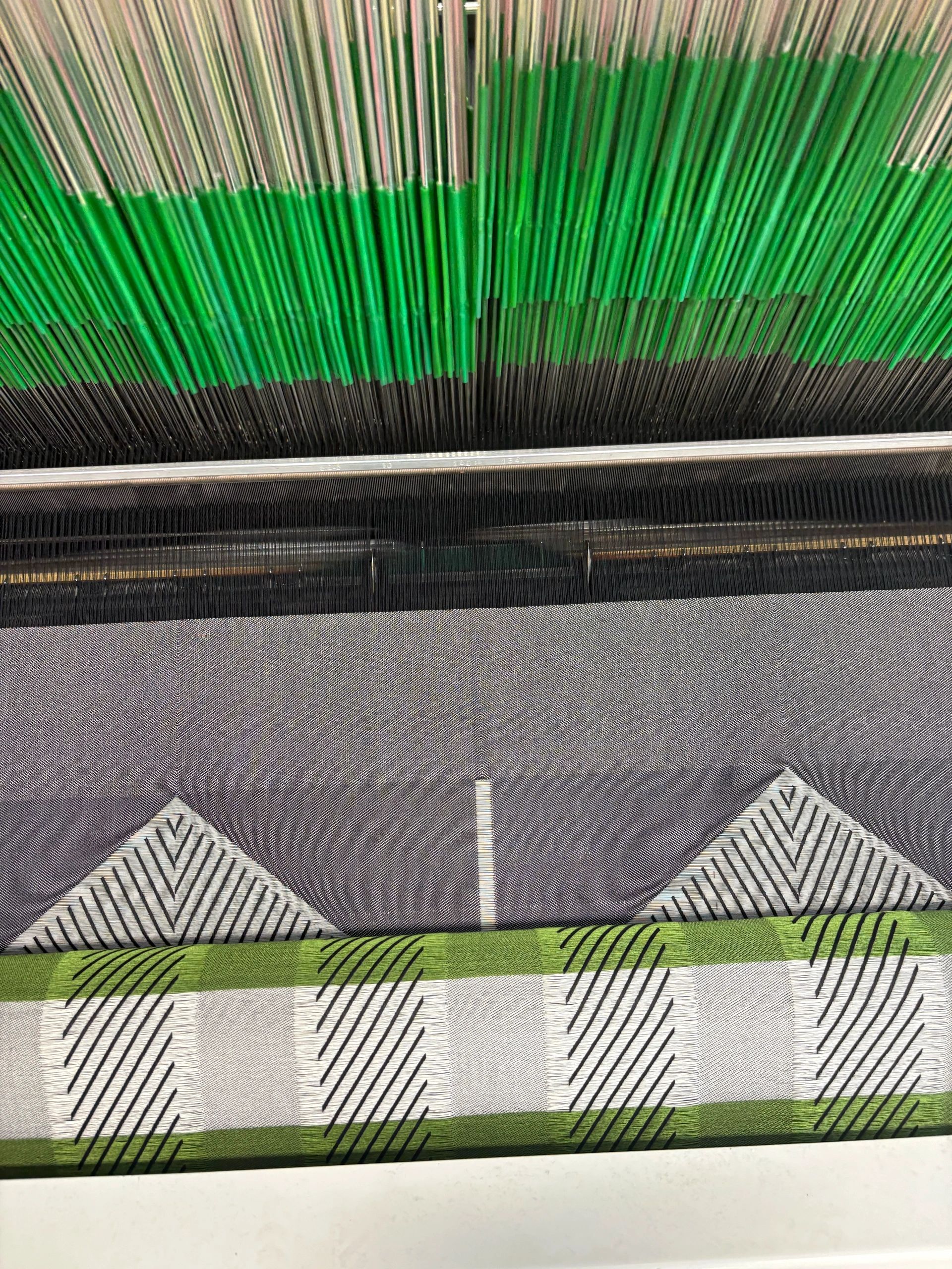 Close-up of a weaving loom creating a patterned fabric with green and gray threads.