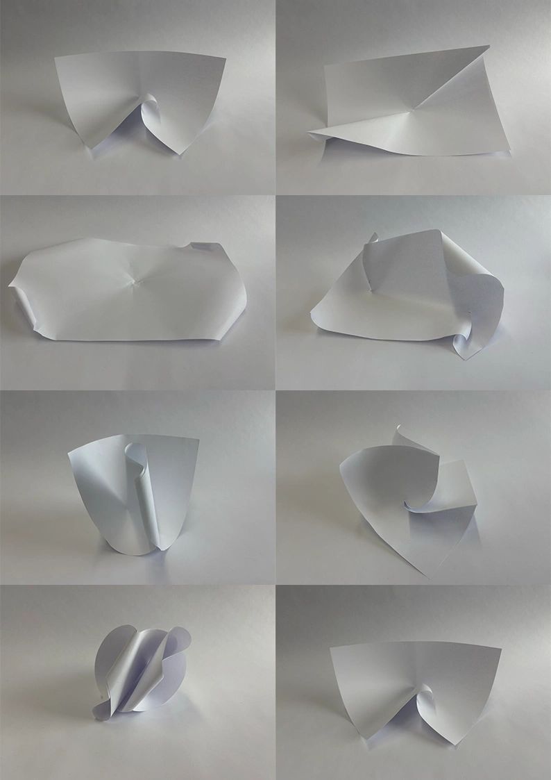 Various abstract shapes formed by folding white paper on a plain background.