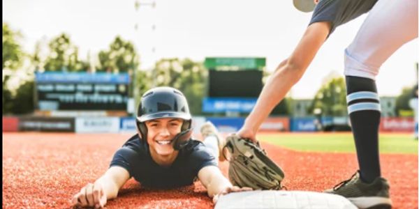 Happy baseball player sliding to a base with teammate ready to tag.