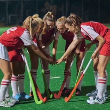 Female field hockey players putting hands together in a team huddle.