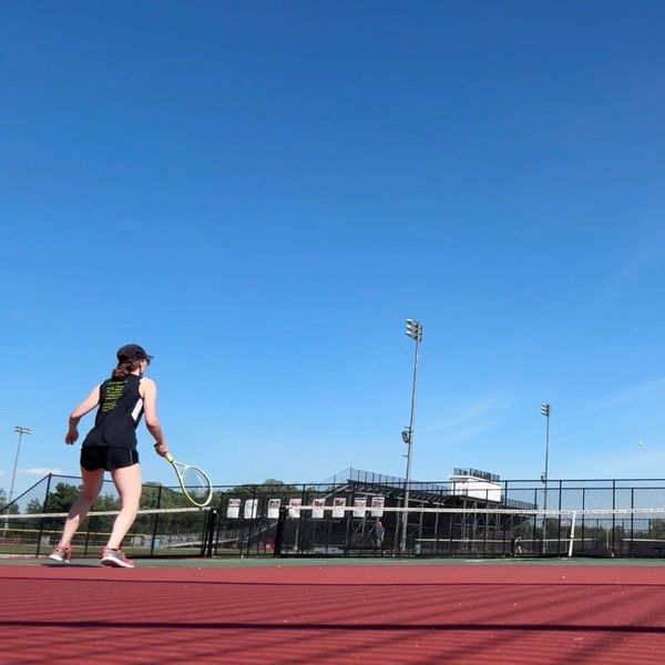 Person playing tennis on an outdoor court under a clear blue sky.