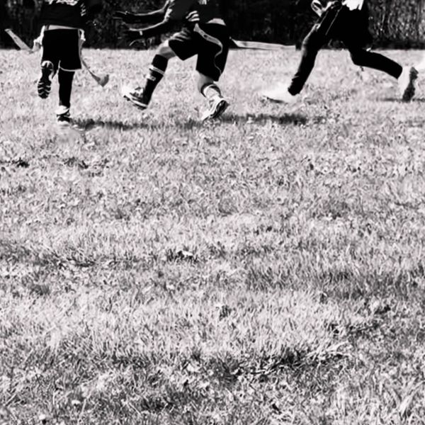 Kids running on grass with sticks in hand.