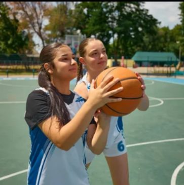 Two girls preparing to shoot a basketball on an outdoor court.