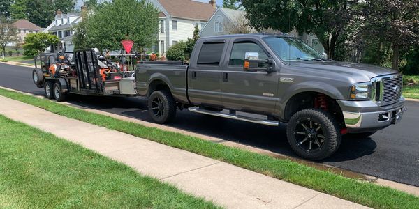 A gray Ford F-250 truck towing a trailer loaded with landscaping equipment.