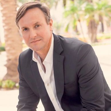 White male, Michael Waddington, pictured behind a large palm tree and distant palm trees