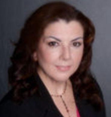 white female, Stephanie Story, pictured behind a blurred background wearing black blazer and red nec