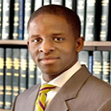 African American male, Tony Luti, pictured behind legal books wearing a brown blazer.