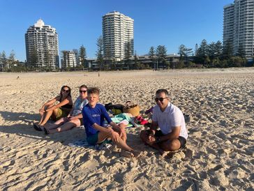 Family relaxing on a sunny beach with city buildings in the background.