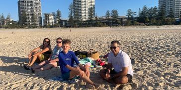 Family relaxing on a sunny beach with city buildings in the background.