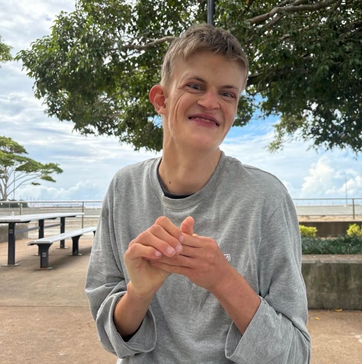 Happy young man smiling outdoors near benches and trees.