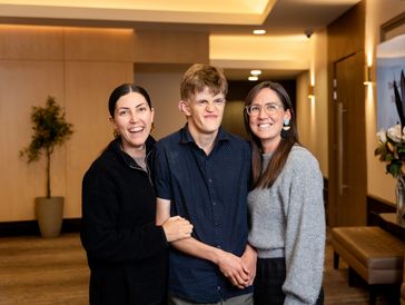 Three people smiling and posing together in a warmly lit indoor setting.