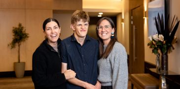 Three people smiling and posing together in a warmly lit indoor setting.