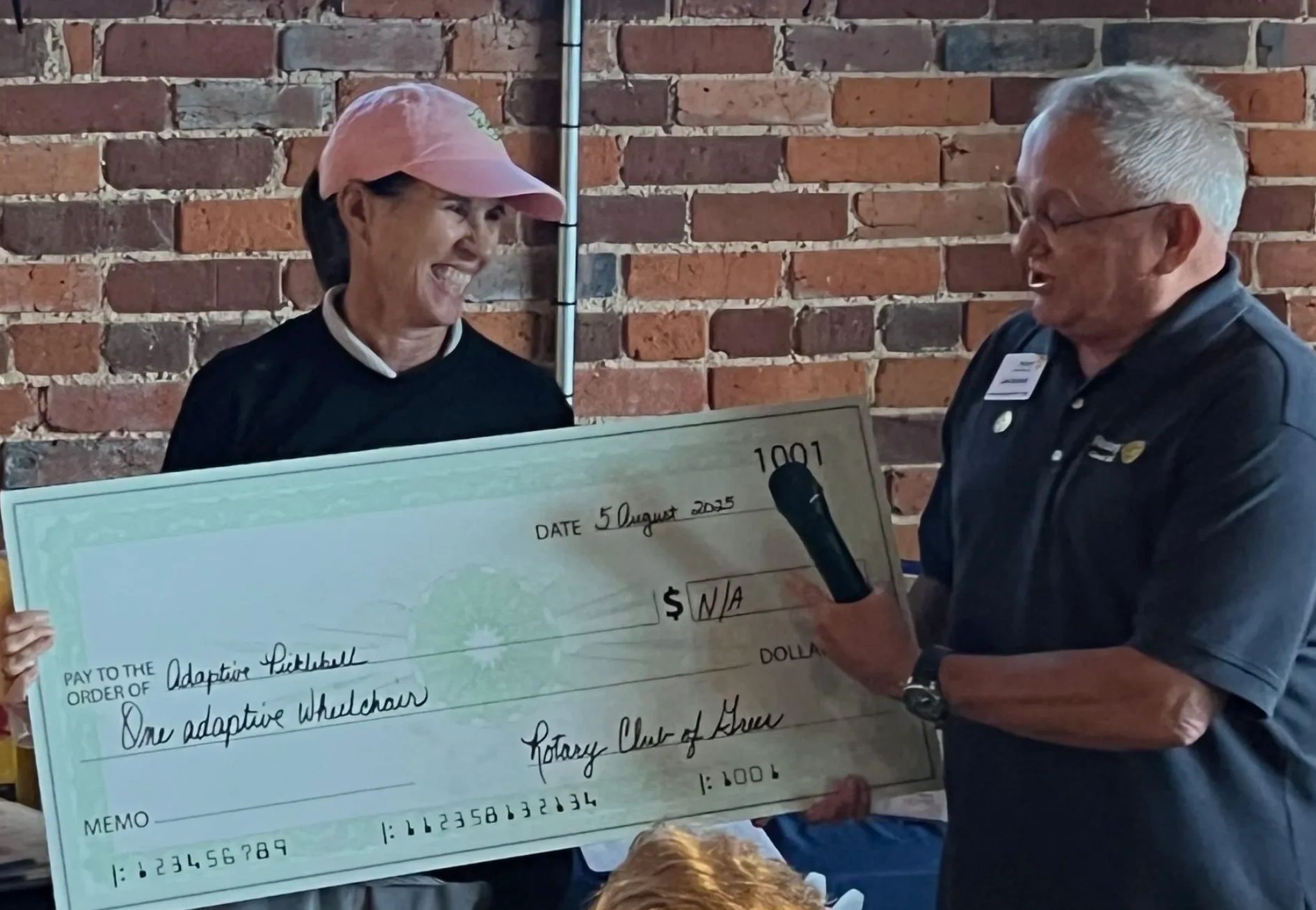 Two people holding a large check for an adaptive wheelchair donation.