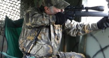 Man in a ground blind using a Hip Stick Shooting Rest on his hip to steady his rear arm with a rifle