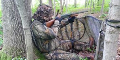 Turkey hunter sitting at a tree using a Hip Stick Shooting Rest on his knee to steady his shotgun