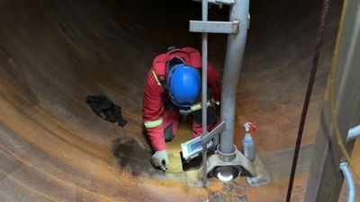 Worker in protective gear inspecting inside a large industrial pipe.