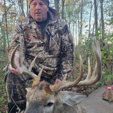 Hunter in camouflage holding a large buck's antlers in the forest.
