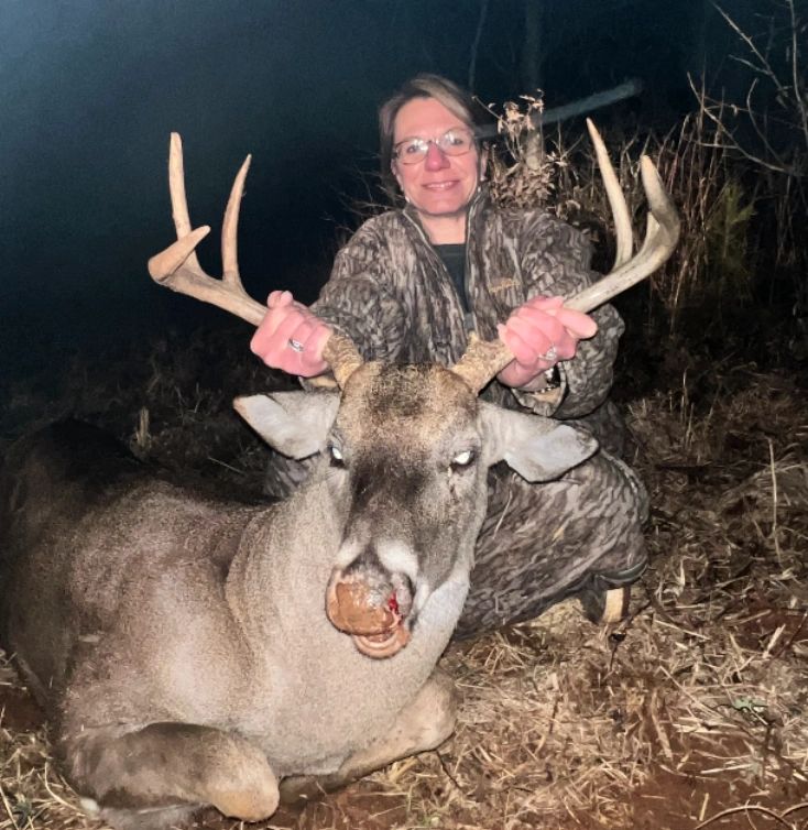 Hunter posing with a large buck deer at night.