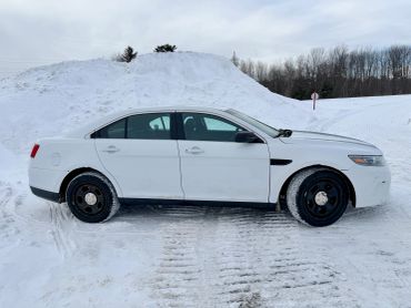 White sedan parked on a snowy ground with snow piles in the background.