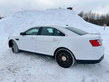 White sedan parked on snowy ground with snowbanks in the background.