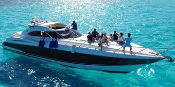 A yacht with people enjoying on turquoise water near a city skyline.