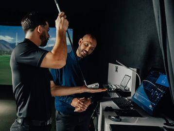 Two men analyzing golf club data on a computer indoors.
