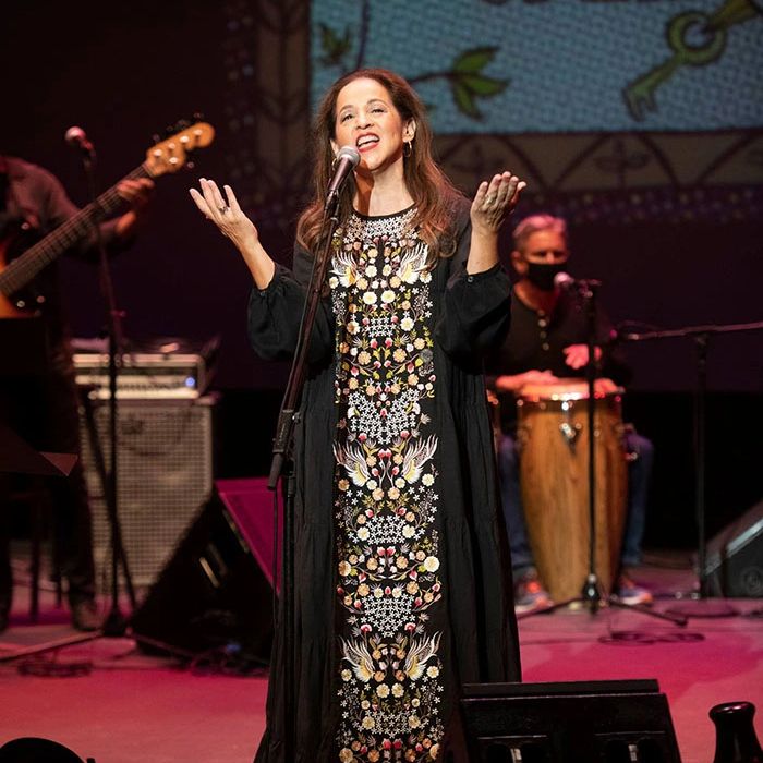 Woman singing on stage with musicians in the background.