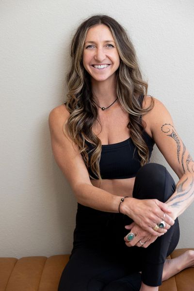 Smiling woman with long wavy hair and arm tattoo sitting comfortably.