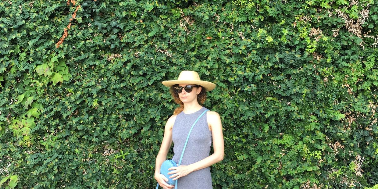 Woman with straw hat and grey jersey maxi dress standing outside in front of lush green ivy 