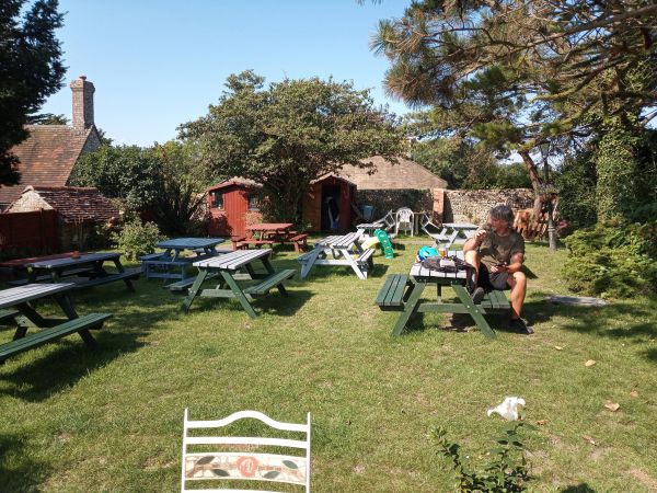 A man sitting alone on a picnic table in a sunny garden area.