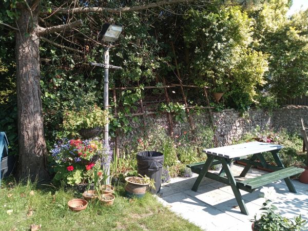 A sunny garden corner with a picnic table, flowers, and a lamp post.