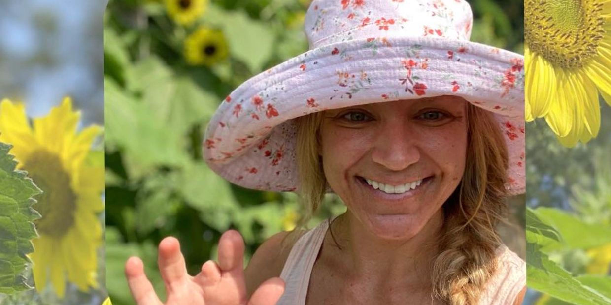 Jennifer Haddock, site owner, stands in her sunflower field, waving to the camera. 