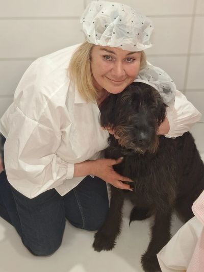 Woman in white hairnet hugging large black dog indoors.
