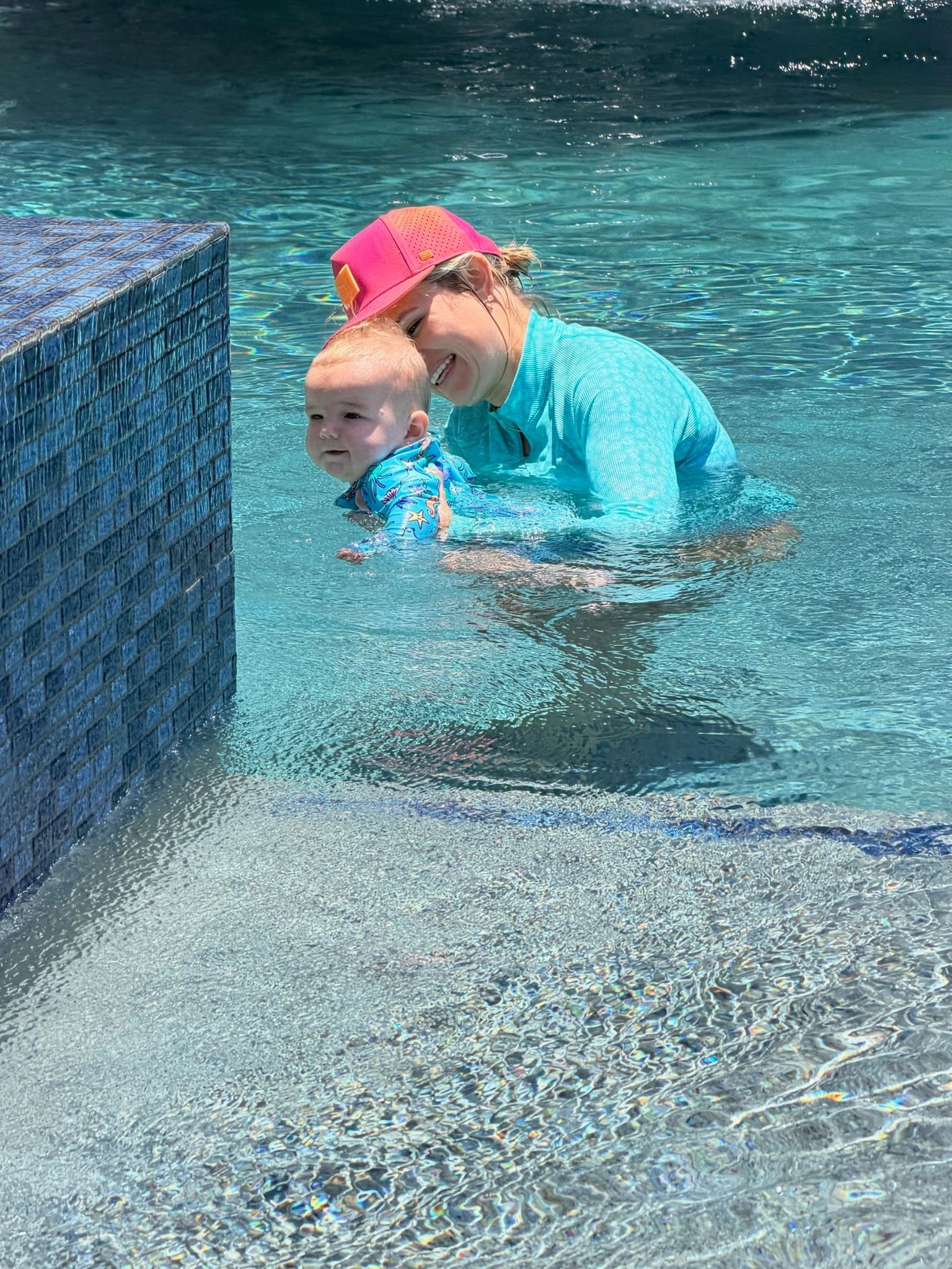 Woman joyfully holding a baby in a swimming pool.