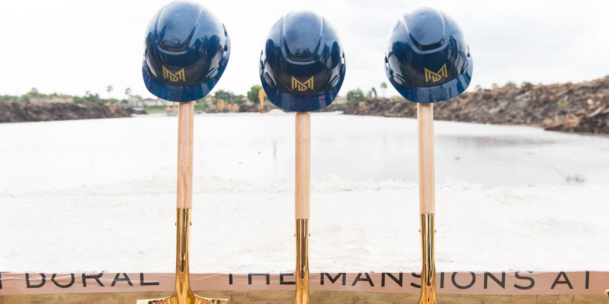 Three golden shovels with blue helmets on top at a construction site.