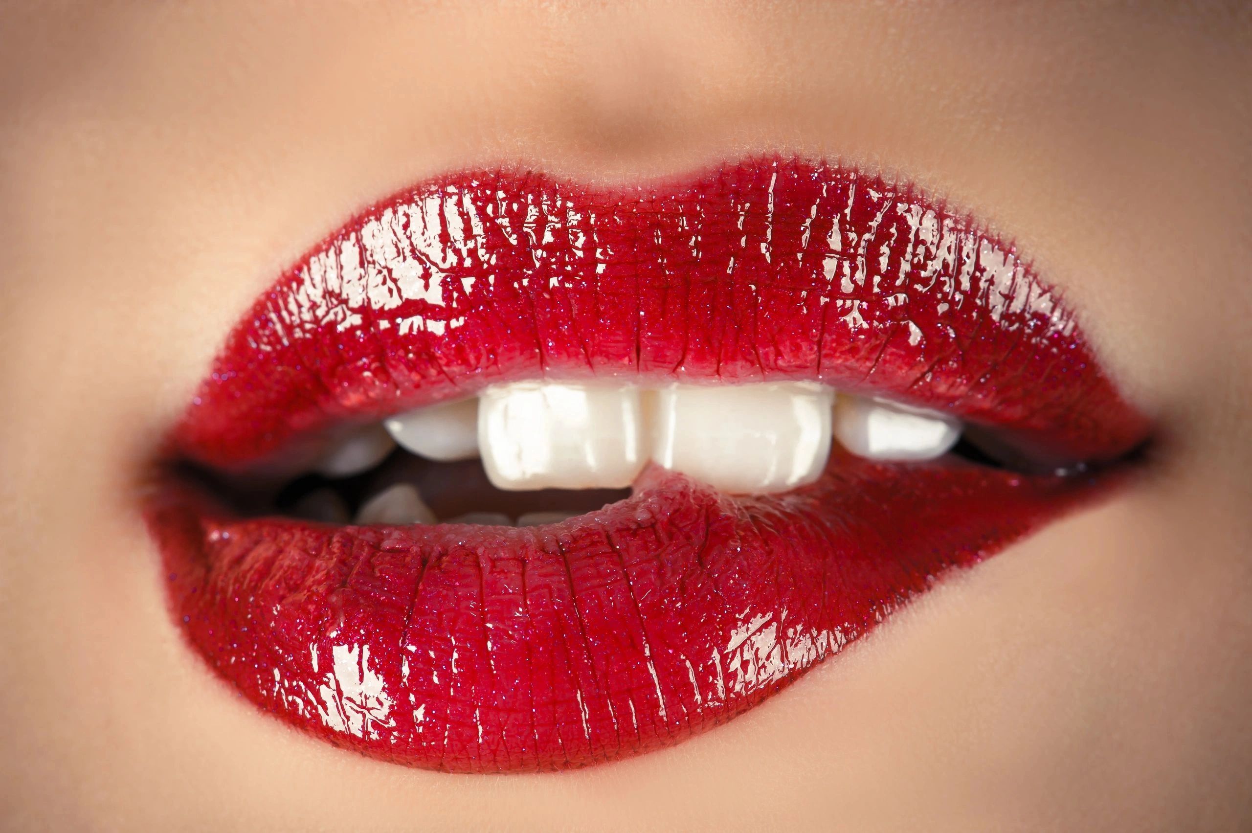 Glossy red lips biting the lower lip sensually.