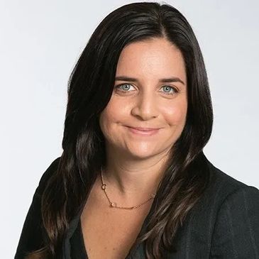 Professional woman with dark hair and blue eyes smiling gently.
