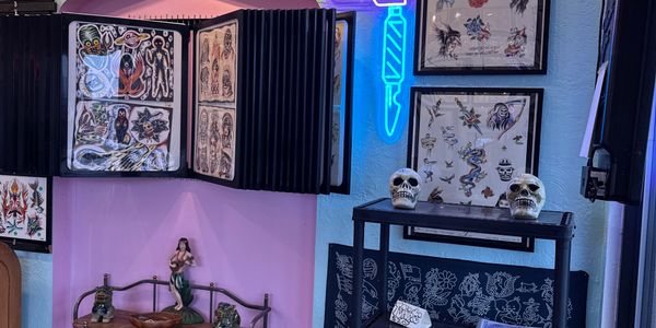 Tattoo studio corner with flash art, skull decor, and neon knife light.