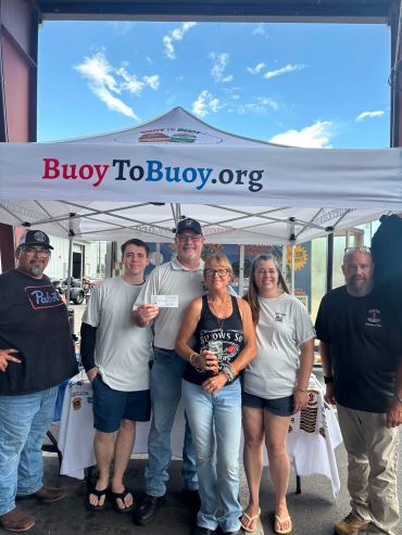 Group of five people standing under a BuoyToBuoy.org tent.