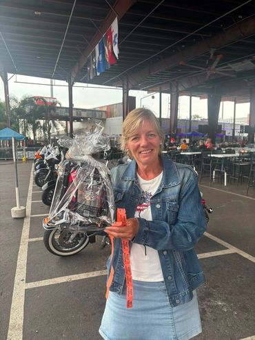 Woman holding a wrapped gift and smiling in a covered outdoor area.