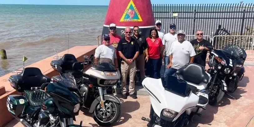 Group of people posing with motorcycles near a waterfront buoy.