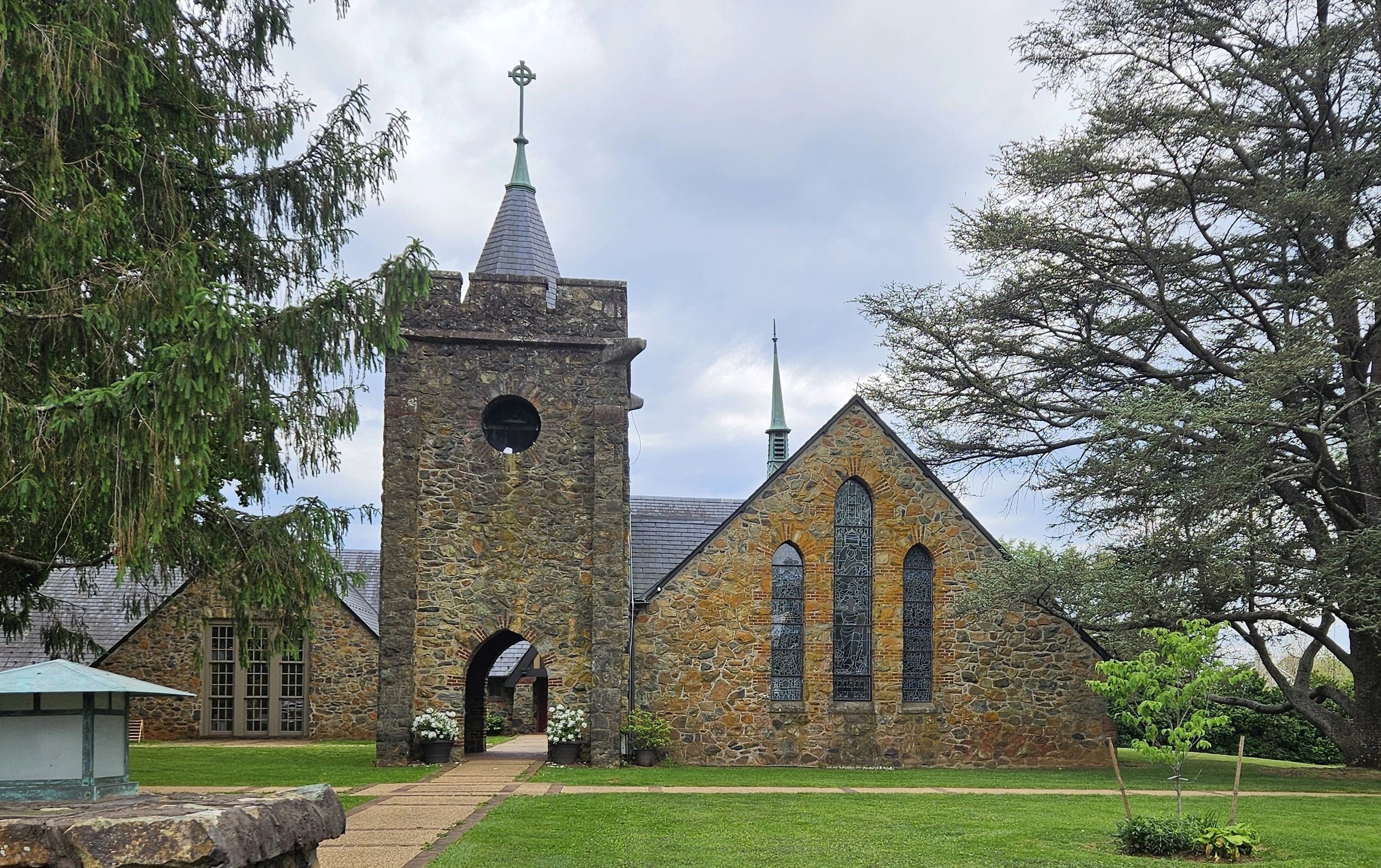Stone church with stained glass windows and a bell tower under a cloudy sky.