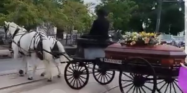 A horse-drawn carriage carrying a coffin with flowers.