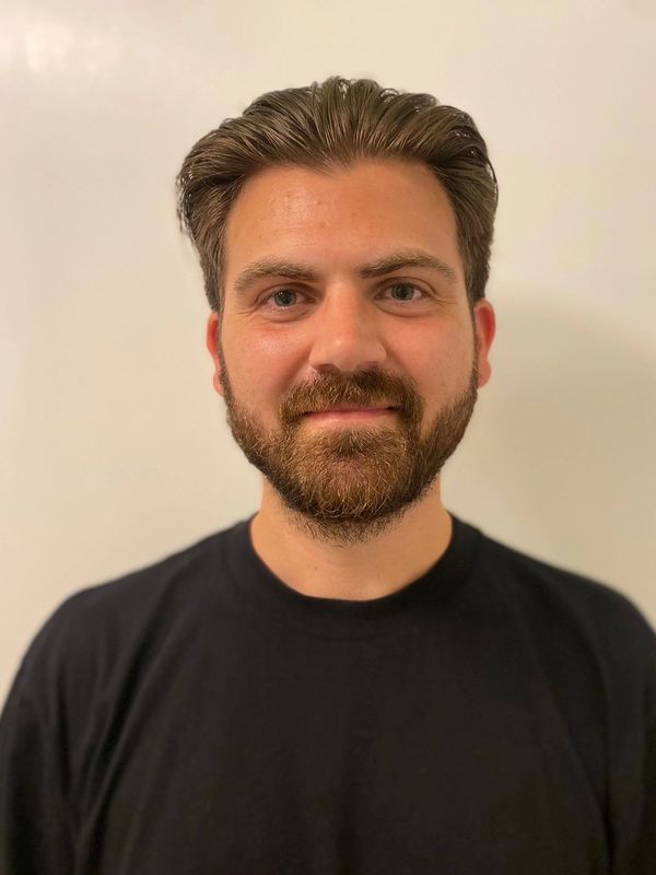 Smiling man with neatly styled hair and beard in a black shirt.