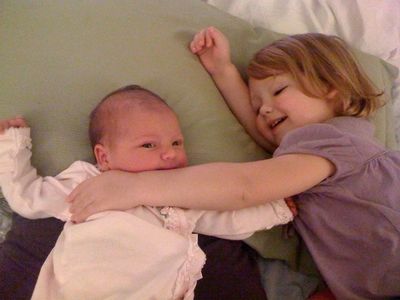 A little girl hugging her baby sibling while they lie together on a pillow.